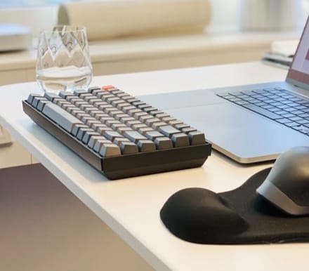 Keyboard set up on a table with a glass of water, mouse and laptop